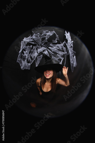 portrait of a young witch in hat on black background with spider net