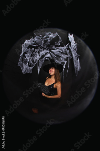 portrait of a young witch in hat on black background with spider net