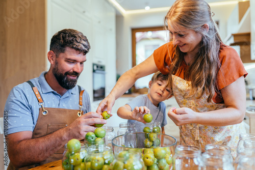 Parents and little son canning greengage plums together at home kitchen table