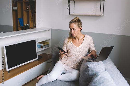 Fotomural Focused freelancer multitasking with laptop and smartphone while working remotel