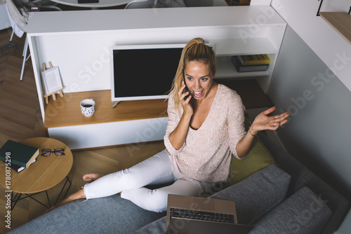 Fotografía Freelancer animatedly speaking on phone while working remotely, gesturing expres