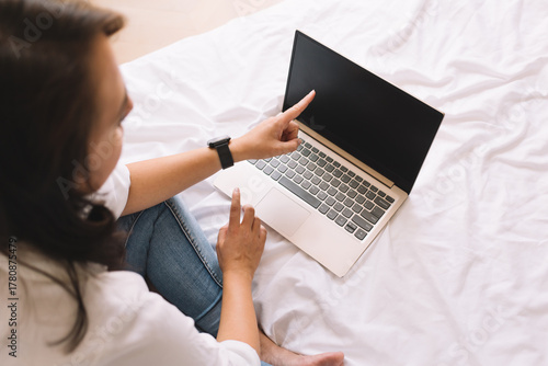 Cuadro en lienzo Woman sitting on bed pointing at blank laptop screen, symbolizing pause, decisio