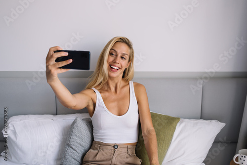 Cuadro en lienzo Woman taking selfie with smartphone while smiling in bed, capturing digital self