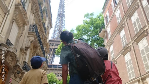 Family travelers — father and two children looking up at the eiffel tower from a paris street, surrounded by classic haussmann buildings on a sunny summer day exploring together