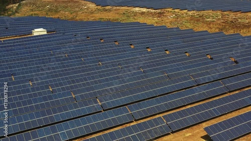 Drone shot of solar panels on ground at solar power farm under blue sky, providing renewable electricity surrounded by fence and natural landscape promoting eco friendly energy for sustainability