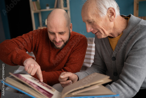 Happy fathers day concept. adult son with his old elderly senior father looking family photograph photo at home.