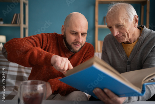 Happy fathers day concept. adult son with his old elderly senior father looking family photograph photo at home.