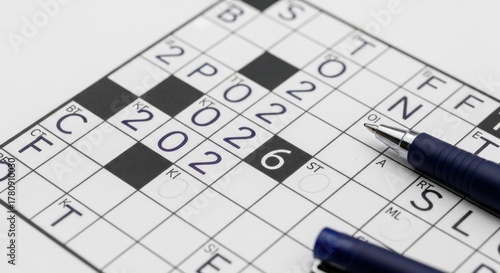 A close-up of a crossword puzzle with partially filled squares and a pen resting on the grid, hinting at a puzzle in progress