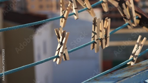 Clothespins hanging on a blue clothesline. The background is blurred, showing a hint of a domestic setting. The scene conveys a sense of everyday life and simplicity.