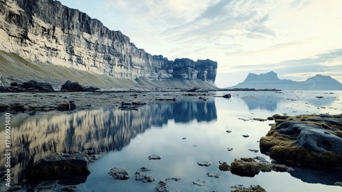 Wallpaper Mural Massive coastal cliffs stand tall above still water reflecting the pale sky and distant peaks Torontodigital.ca