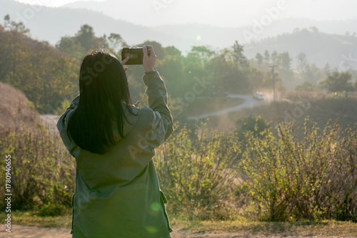 Wallpaper Mural Rear view of a female tourist taking photos of a beautiful sunset on a mountain peak during the cold winter season. Concept of travel, adventure, freedom, and connection with nature. Torontodigital.ca