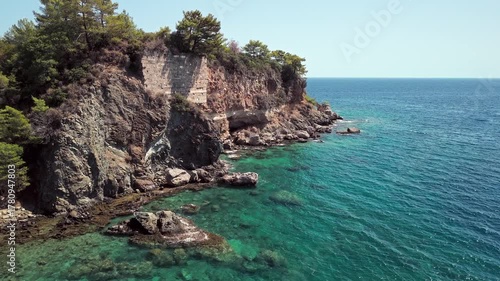 Drone view of the rocky coastline and turquoise waters surrounded by pine forest near Phaselis Bay, Antalya, Turkey. Clear Mediterranean sea and mountain landscape.