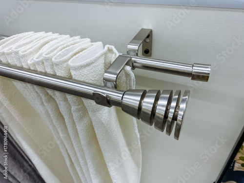 Stainless steel finial on rod, polished chrome detail with curtain pleats and rings, sleek modern finish showcased in showroom sample, emphasis on craftsmanship and contemporary hardware