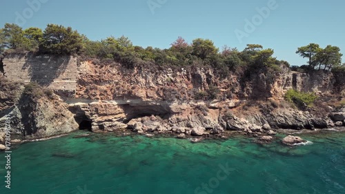 Drone view of the rocky coastline and turquoise waters surrounded by pine forest near Phaselis Bay, Antalya, Turkey. Clear Mediterranean sea and mountain landscape.