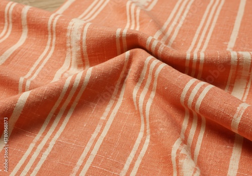 Close up view of a soft orange and white striped textile fabric with natural texture and elegant folds providing a warm background