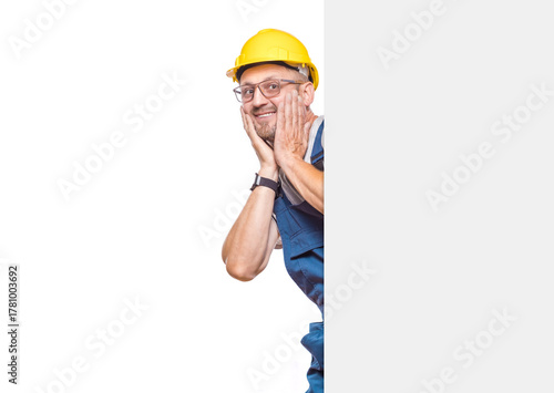 Ecstatic construction worker holding white board, isolated on white background. Handsome repairman showing blank empty paper billboard with blank space for text. Craftsman against white wall