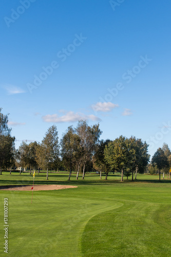 Golf green with sand bunkers and trees under blue sky