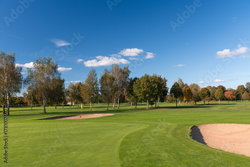 Golf green with sand bunkers and trees under blue sky