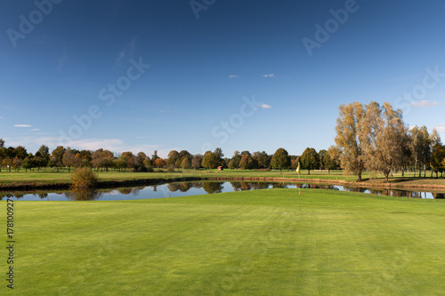 Golf green with flag and pond surrounded by autumn trees