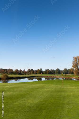Golf green with flag and pond surrounded by autumn trees