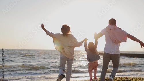 Full body back view young happy parents mom dad with little child kid daughter girl wearing casual clothes rest in free time walk run to sea sand shore beach outdoor in summer day. Family day concept