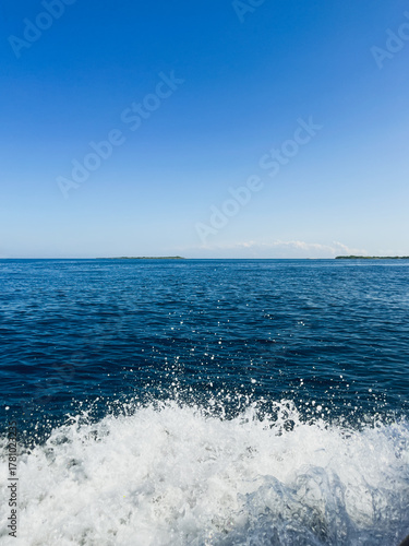 Boat wake splashing on deep blue tropical ocean water - Fast moving water surface with white foam and bright clear sky