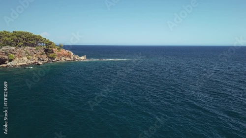 Drone view of the rocky coastline and turquoise waters surrounded by pine forest near Phaselis Bay, Antalya, Turkey. Clear Mediterranean sea and mountain landscape.