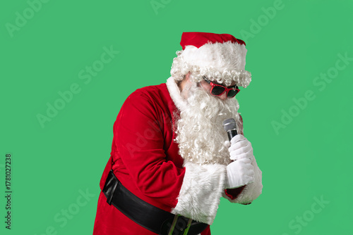 Wallpaper Mural Santa Claus, with a white curly beard, wearing a red suit and sunglasses, sings songs into a microphone and dances cheerfully against a green background. Ideal for Christmas themed compositions. Torontodigital.ca