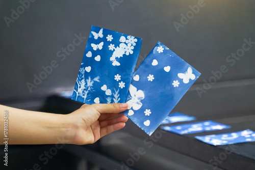 Hand holding two bright blue cyanotype cards featuring butterfly, flower, and heart patterns. Artistic sun printing, craft, and DIY concept.