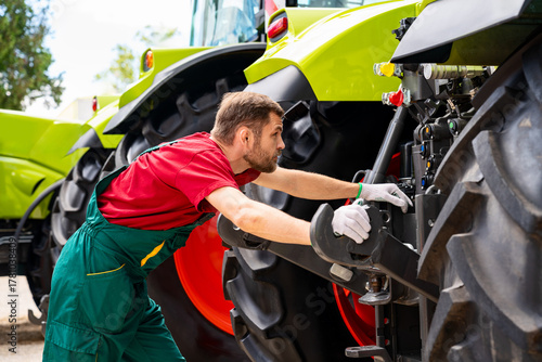 Male agricultural machinery mechanic examining tractor