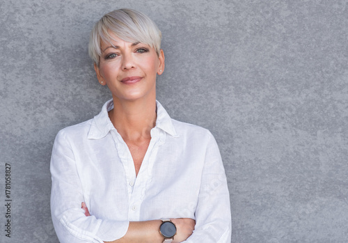 Serious adult woman standing with neutral face expression, against gray background - wall. Pretty middle age woman