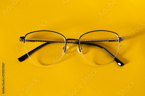 Stylish women’s metal half-rim eyeglasses on a vivid yellow background. Minimalist composition for vision, fashion, optical accessories, or healthcare concepts. Perfect for advertising templates.