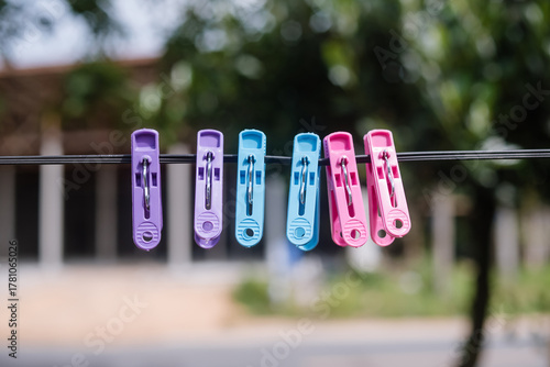 Multi-colored clothespins are attached to a clothesline and the floor is a blurred tree with green leaves.	