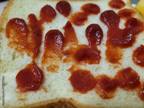 A piece of white bread with red ketchup smears.