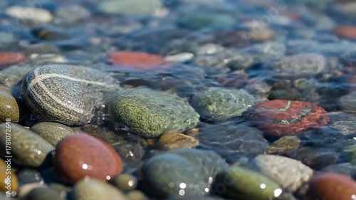 Close up of colorful wet pebbles on a beach with gentle waves washing over them.