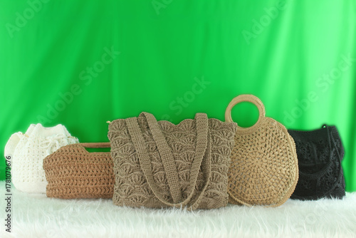 Crocheted bags in different colors and varieties arranged on a white fluffy blanket in front of a green background.