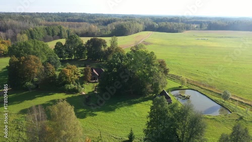 Aerial view of lush green landscape with vibrant trees and serene pond, showcasing gradual camera zoom out revealing expansive fields and natural beauty