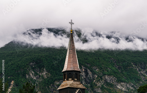 Gjøra Chapel tower stands tall in the village of Gjøra, surrounded by lush green mountains and soft clouds, showcasing its serene Norwegian landscape. In Sunndal, Møre og Romsdal