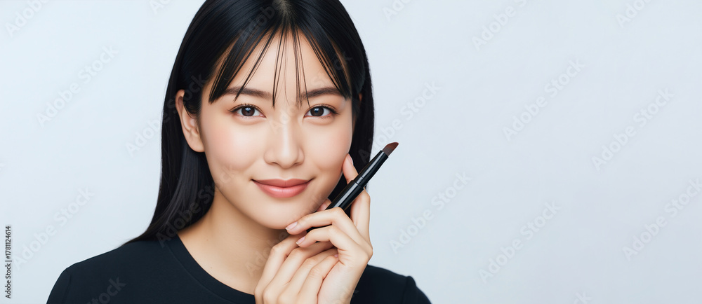 Obraz premium Young Asian woman with natural makeup holding a cosmetic brush. Beauty and cosmetology concept with a smiling model. Skincare advertisement banner with copy space