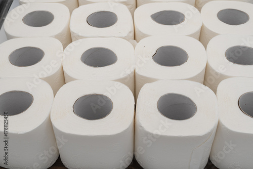 White toilet paper rolls arranged in geometric order on wooden table. Hygiene, sanitation, bathroom supply and cleanliness concept, minimalist product composition.