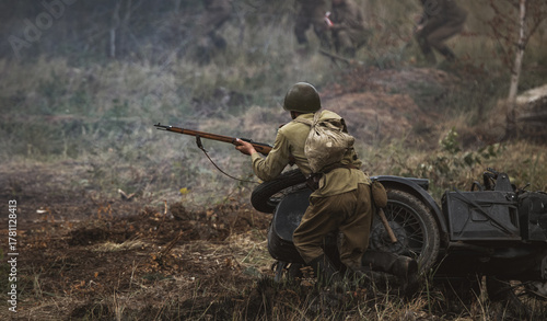 Photography Actor in period-style uniform taking cover and firing a replica rifle during a staged historical battle scene