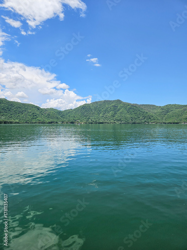 Serene Santa Maria del Oro Lagoon, Nayarit, Mexico. Calm green water reflects the blue sky and clouds. Lush hills create a tranquil natural landscape.