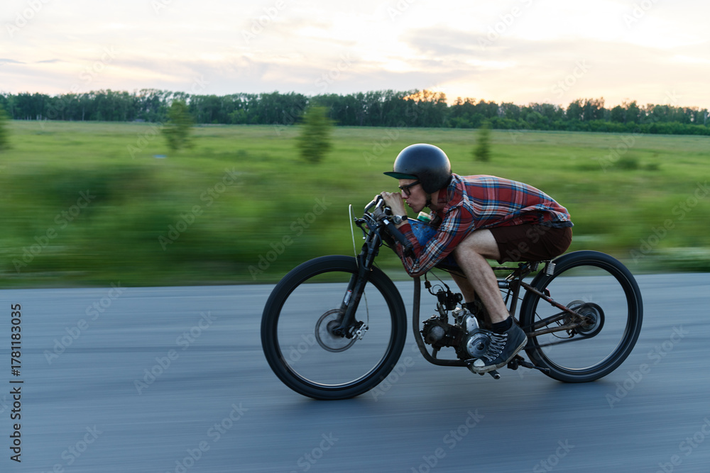 Obraz premium Side view portrait of young hipster man rushing fast on retro bike riding in countryside at dusk