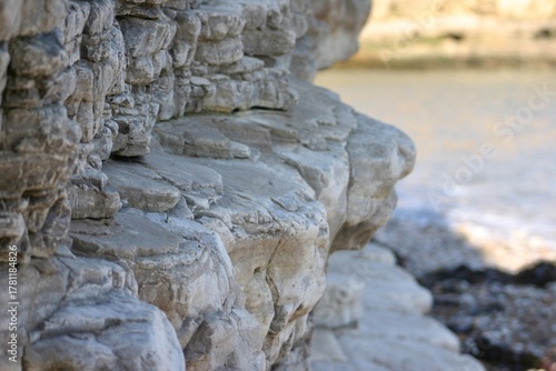 Photos Layered coastal rock formation captured in soft daylight, showing natural erosion, texture, and geological detail near the sea