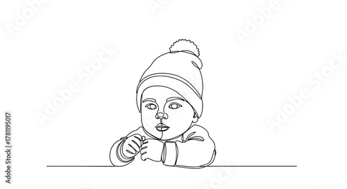 Baby boy wearing winter hat sitting at the table and looking up  