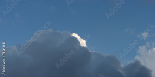 A dark rain cloud covers a white cloud against a blue sky.