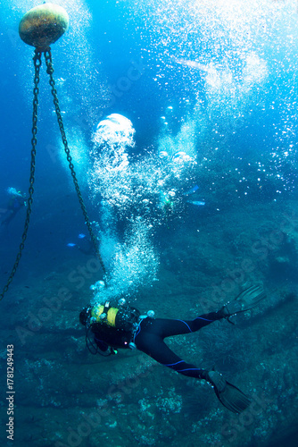 Group of silhouettes of divers at a safety stop at the anchor chain under a boat in the sea.