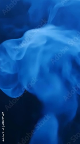 Thick blue smoke curls upward forming soft abstract patterns as it moves gently in dark air creating moody atmospheric motion and calm visual composition