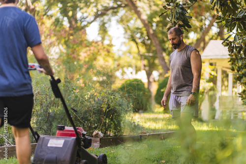 Man is looking down as boy is pushing lawnmower