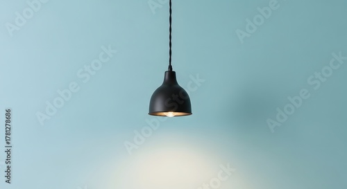 Modern black pendant light hanging from ceiling illuminating a blue wall